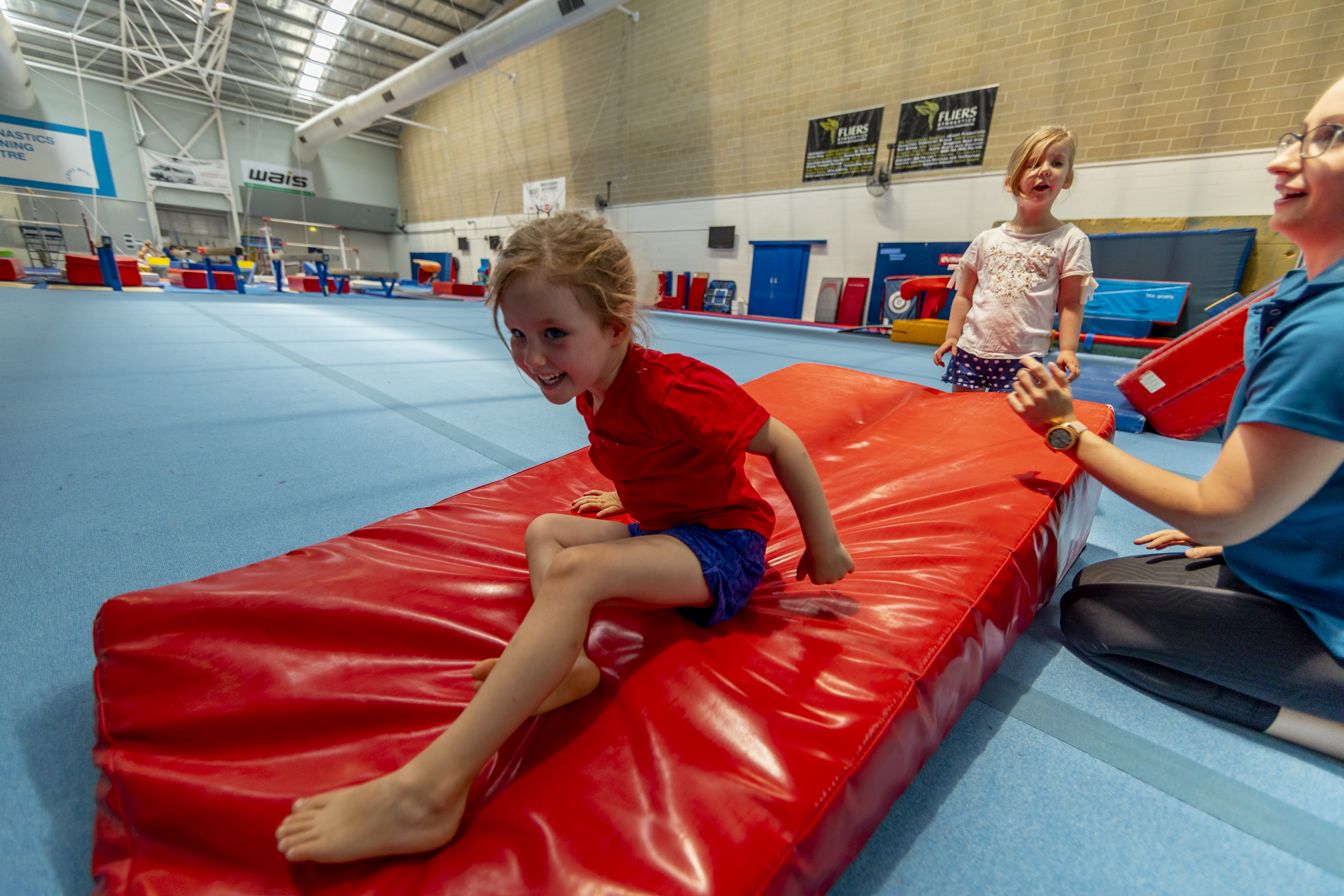 Photo, kid landing on a gymnastics landing mat with another child and teacher looking on