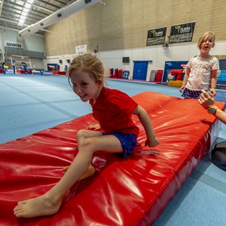 Photo, kid landing on a gymnastics landing mat with another child and teacher looking on