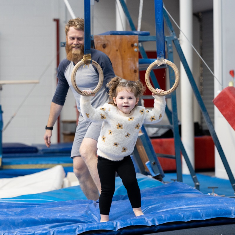 Father watching daughter on the rings at pre-kindy gym