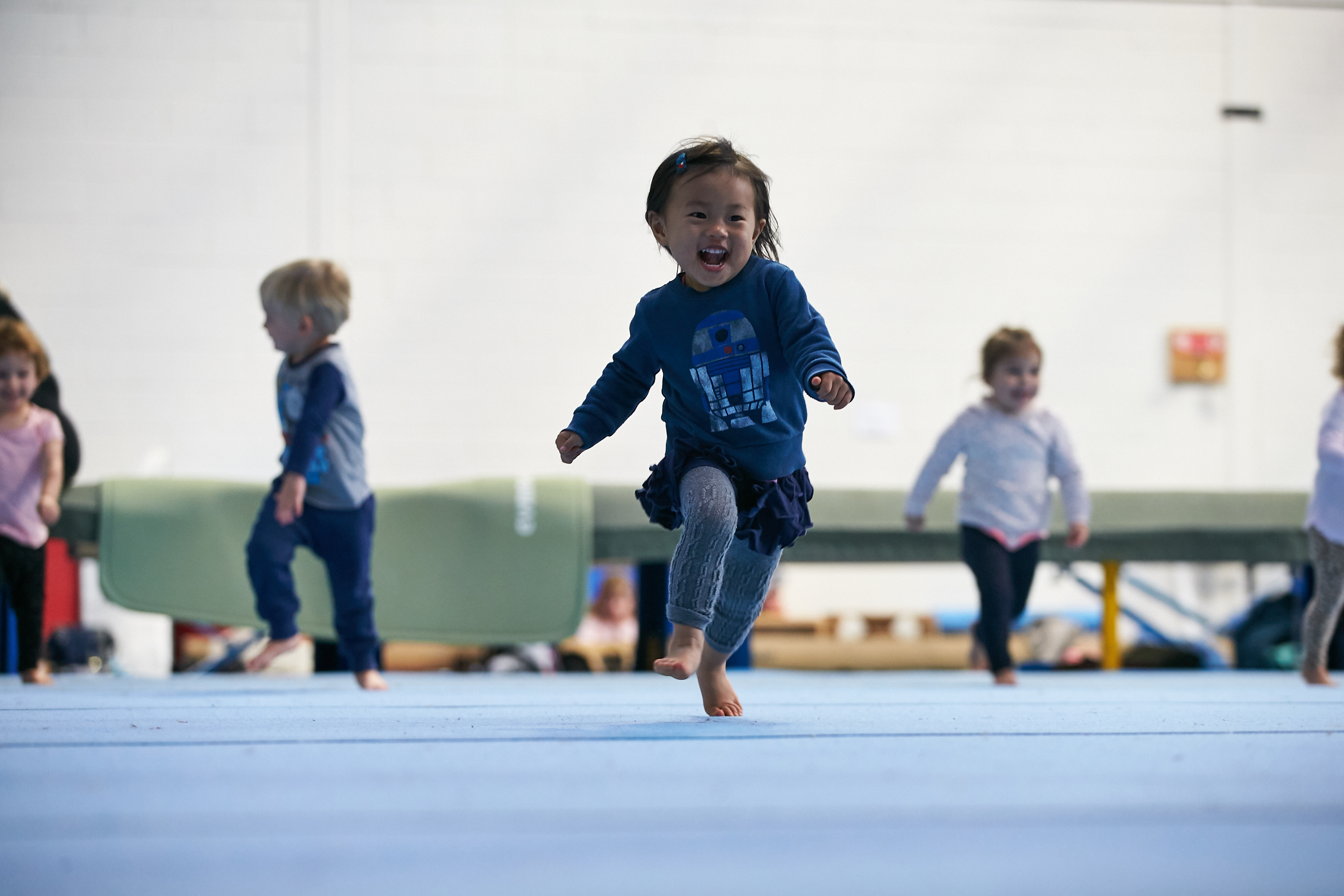 Happy young girl running on floor mat at kids gymnastics