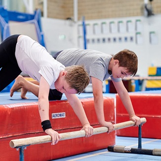 Two kids stretching out onto a gymnastics low bar at the HBF Stadium Kids Gymnastics in Mount Claremont, Perth